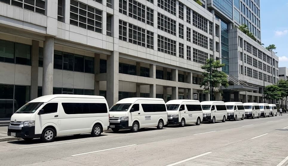 Row of white vans parked on a city street in front of a large building.