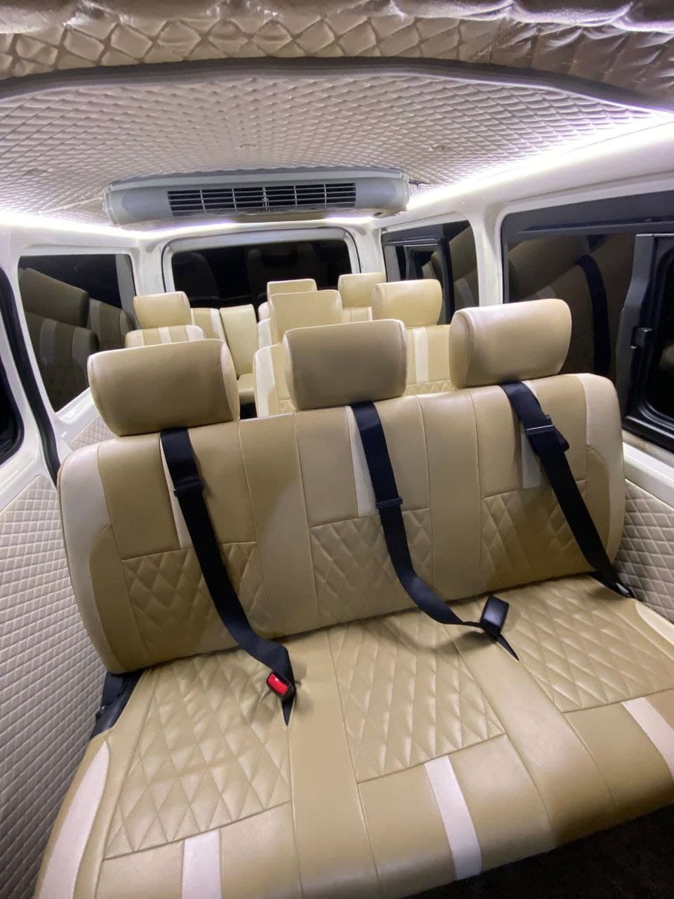 Interior of a luxury van with beige quilted leather seats and bright LED ceiling lighting.