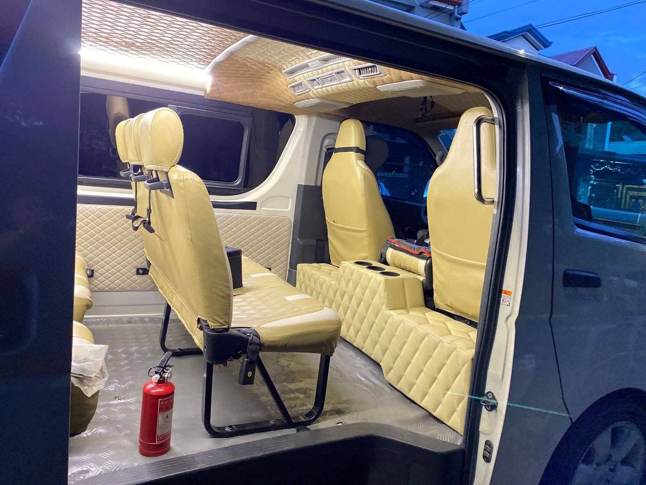 Custom van interior with cream quilted leather upholstery on seats and walls, warmly lit.