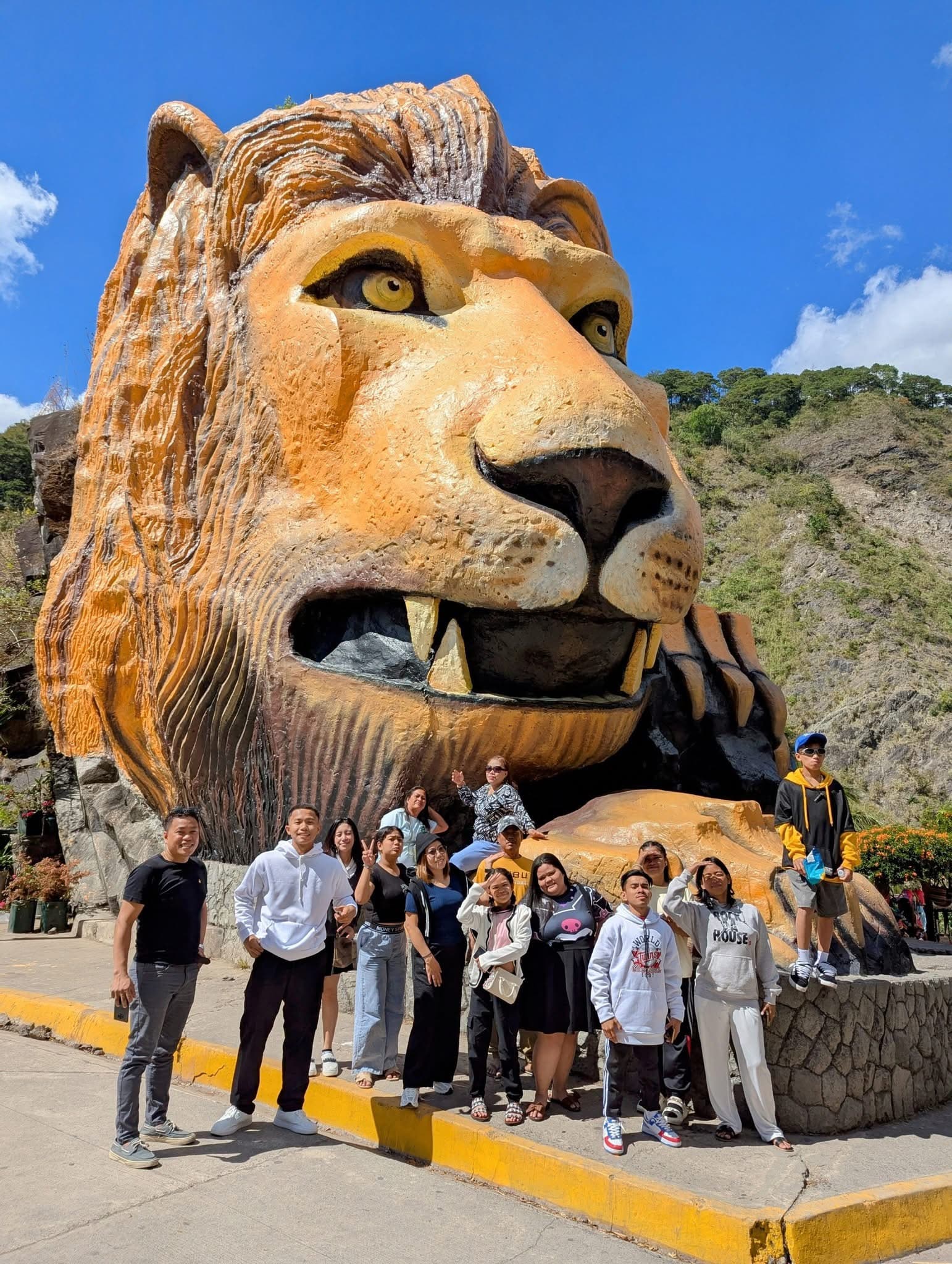 A group of people posing in front of a massive, orange lion head statue outdoors.