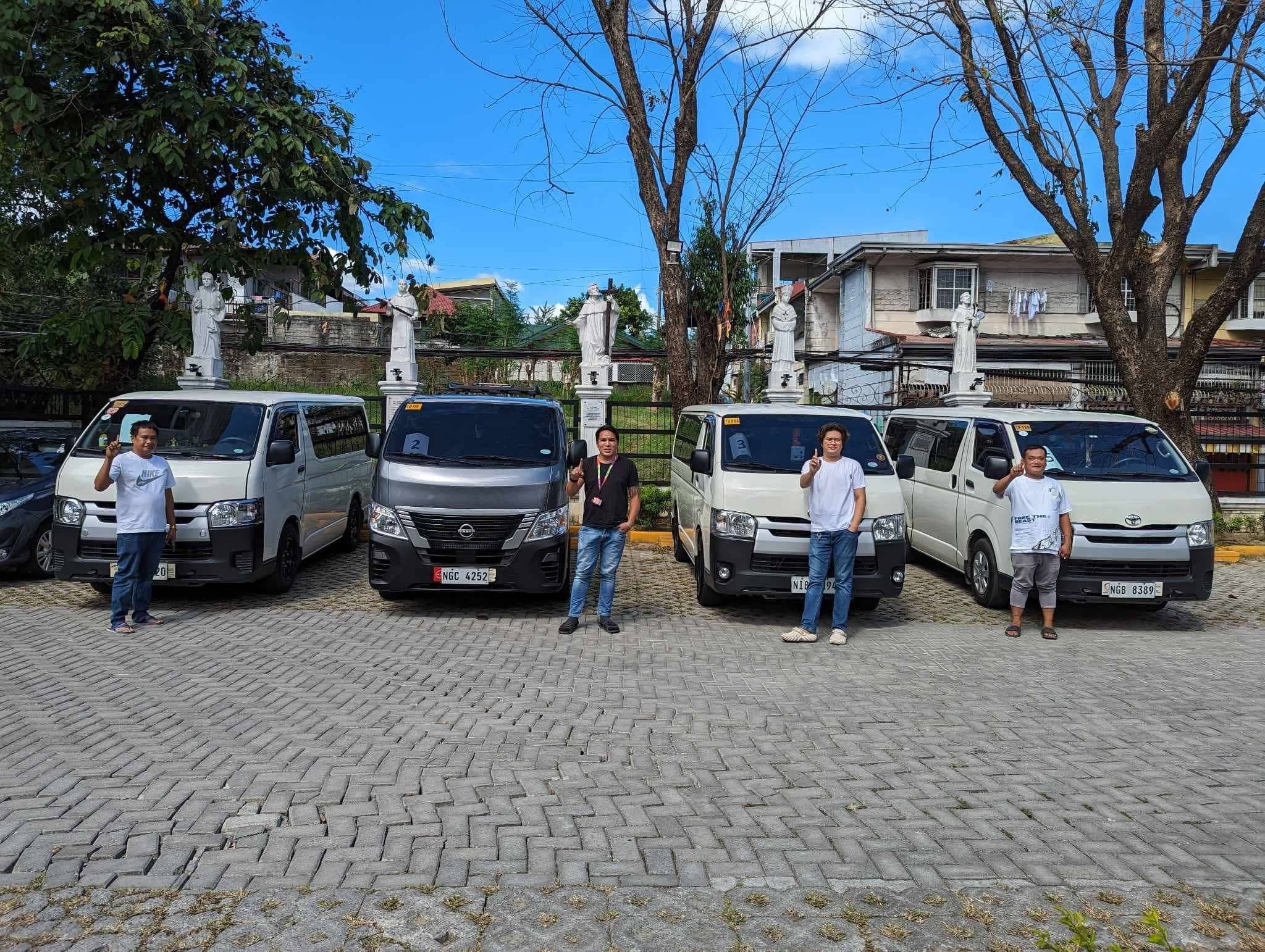 Four men stand in front of four vans in a courtyard with white religious statues.